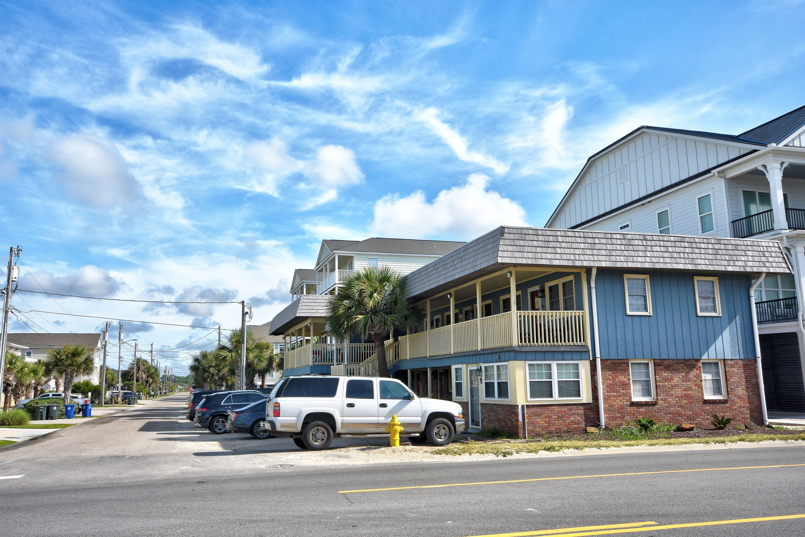 A street view with a two-story building featuring a balcony, parked cars, and a clear sky.