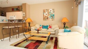 A living room with a sofa, two chairs, a coffee table, and a kitchen area in the background. - Silver Palm Retreat (Kissimmee)
