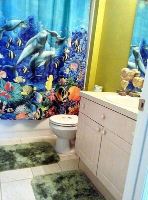 A bathroom with a dolphin-themed shower curtain, a toilet, and a sink with a decorative item on the counter. - Silver Palm Retreat (Kissimmee)