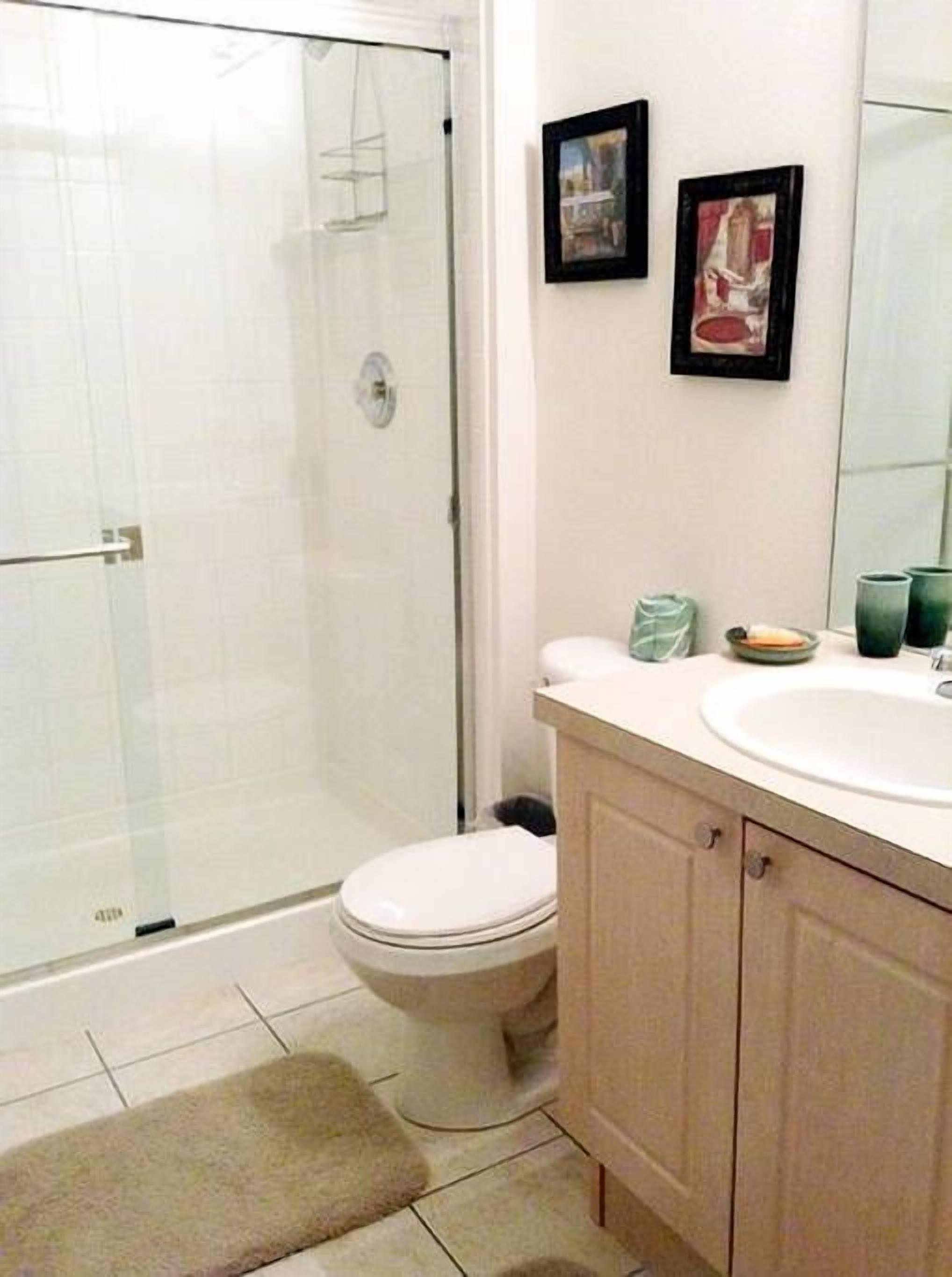 A bathroom with a toilet, a sink, and a shower. There are two framed pictures on the wall.