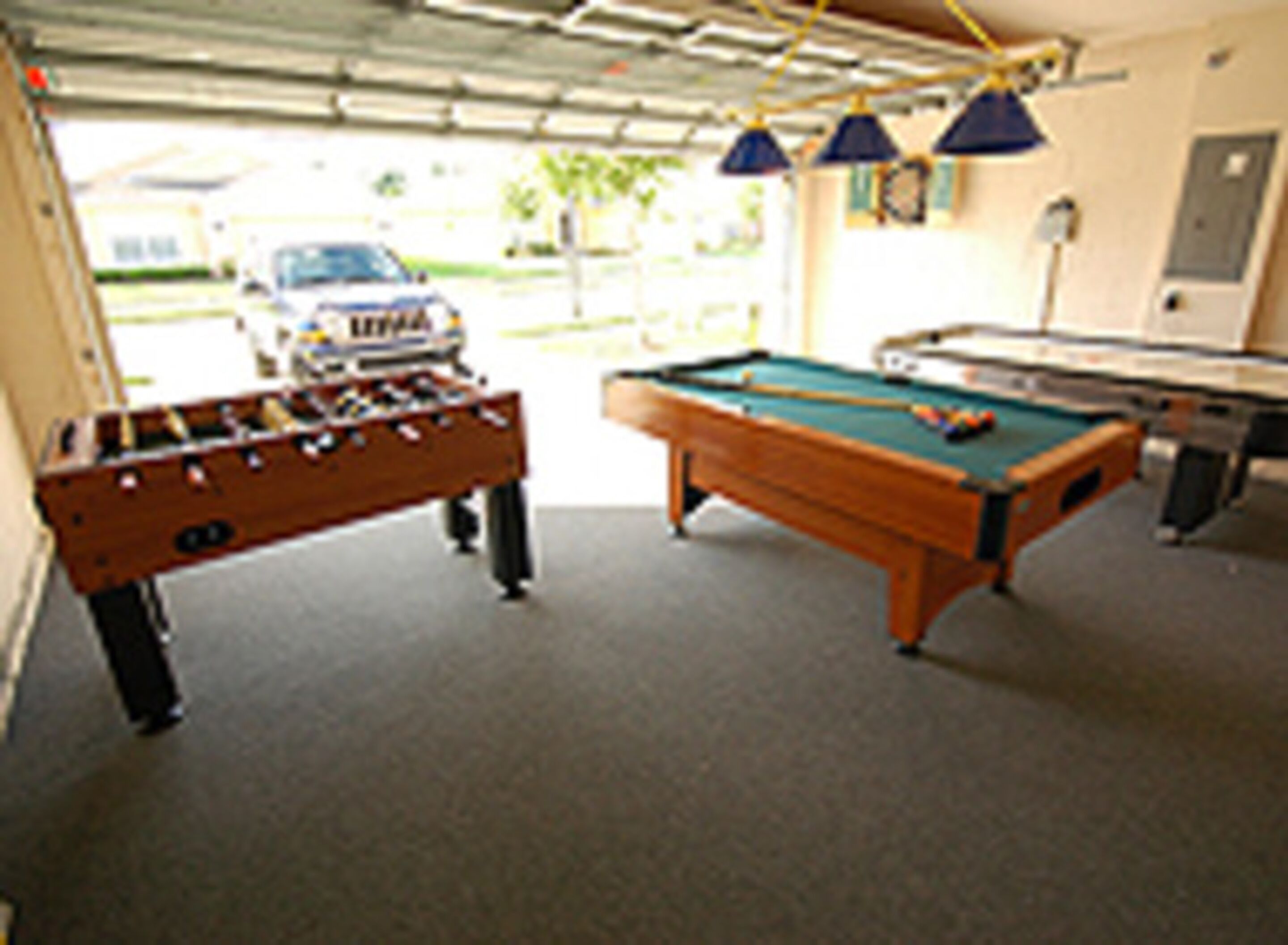 A room with a foosball table, pool table, and a car parked outside.