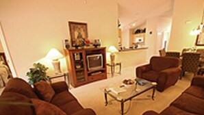 A living room with brown sofas, a coffee table, a TV stand with a TV, and a framed picture on the wall. - Fun Florida Villa (Davenport)