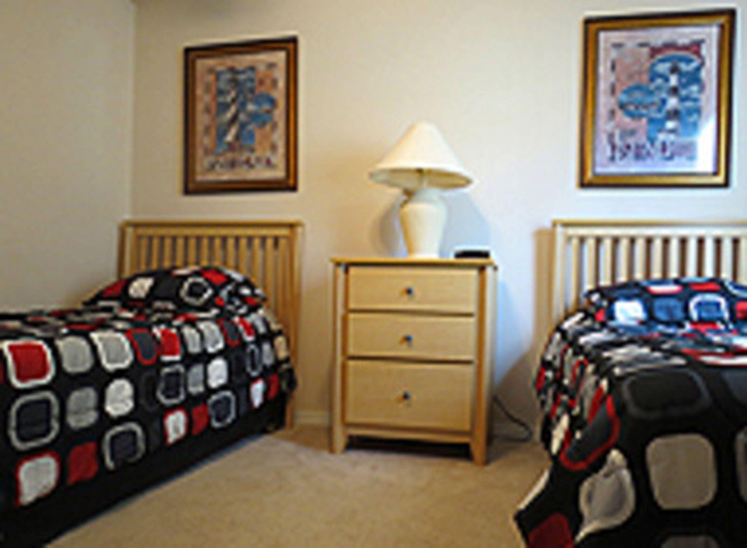 A bedroom with two single beds, a nightstand, a lamp, and two framed pictures on the wall.