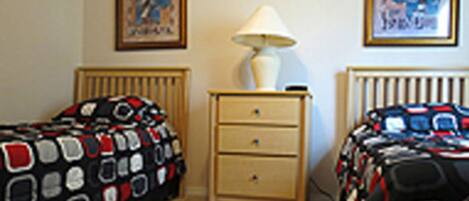 A bedroom with two single beds, a nightstand, a lamp, and two framed pictures on the wall.