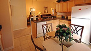 A kitchen with wooden cabinets, a refrigerator, a dining table with chairs, and a potted plant. - Fun Florida Villa (Davenport)