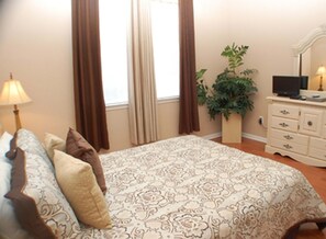 A bedroom with a bed, a dresser, a lamp, a plant, and a window with curtains. - Ridge Castle (Davenport)