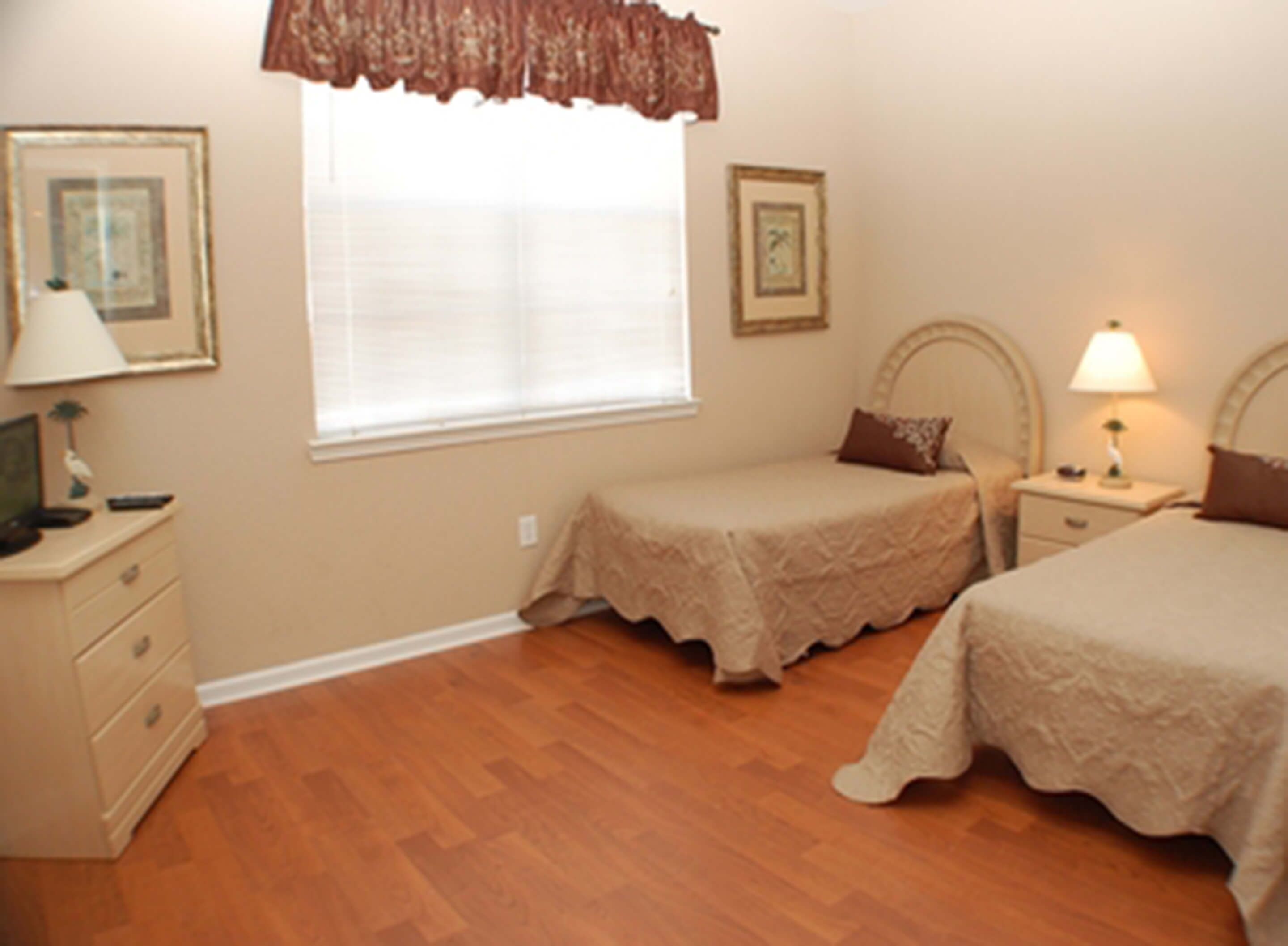 A bedroom with two single beds, a nightstand with a lamp, a dresser, and a window with blinds.