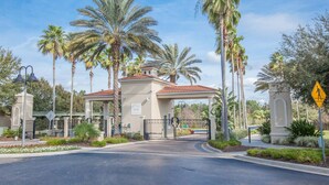 A gated entrance with a red-tiled roof, palm trees, and a clear sky. - Jewel in the Crown (Kissimmee)
