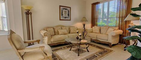 A living room with two sofas, a coffee table, a floor lamp, and a large window with curtains.