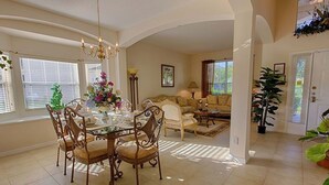 A dining area with a glass table surrounded by ornate chairs, a chandelier, and a floral centerpiece. - Jewel in the Crown (Kissimmee)