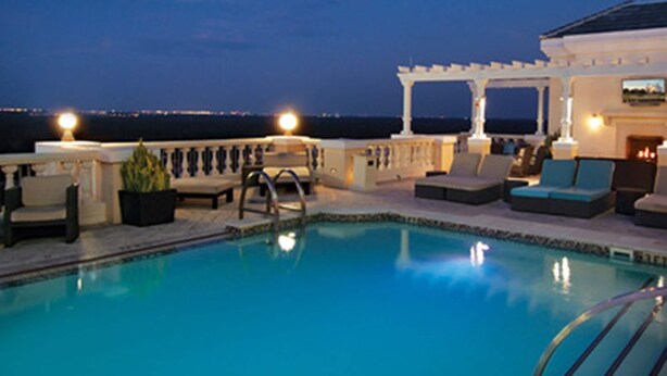 A rooftop pool area with lounge chairs and a pergola, overlooking a cityscape at dusk. - Heritage Haven (Kissimmee)