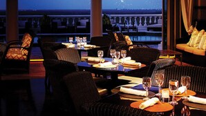 A dining area with tables set for two, chairs, and a view of fireworks in the distance. - Heritage Haven (Kissimmee)
