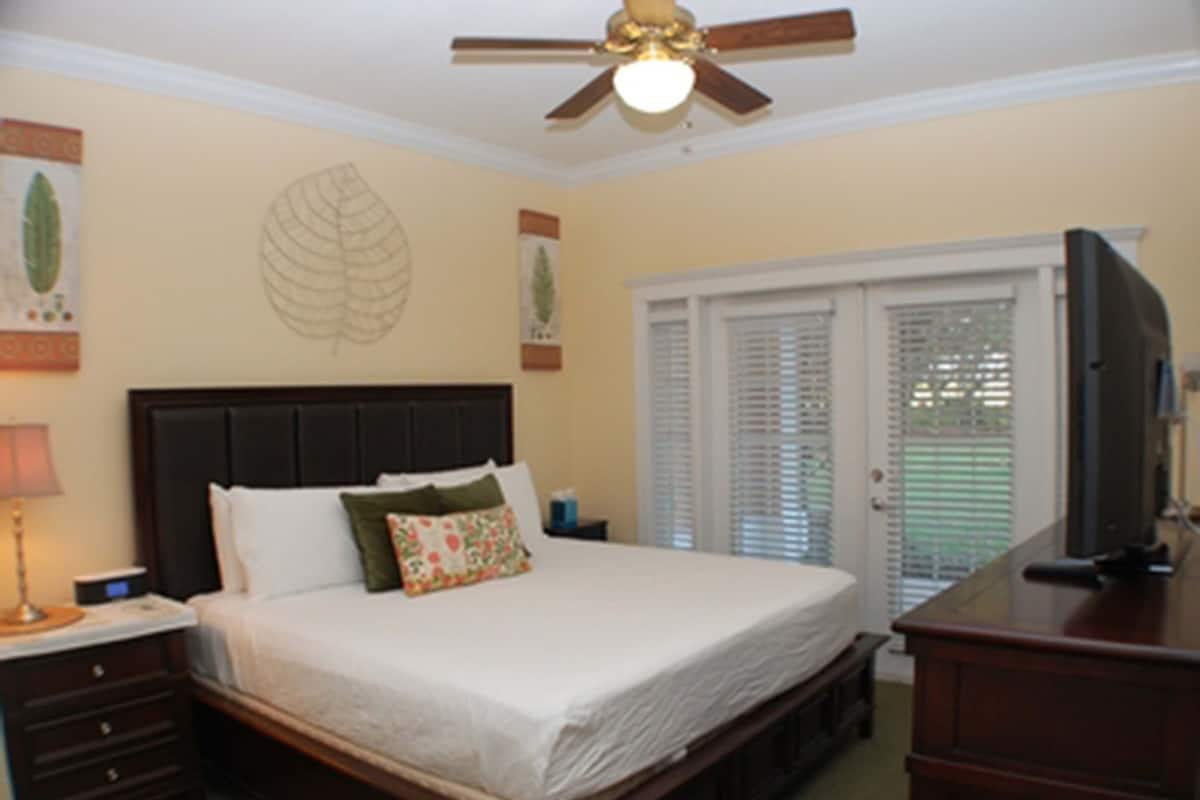 Quarto com cama, mesa de cabeceira, cômoda, ventilador de teto e televisão.