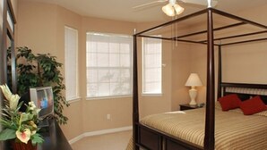 Ein Himmelbett mit Baldachin, ein Nachttisch mit Lampe und ein Blumentopf auf einer Kommode.