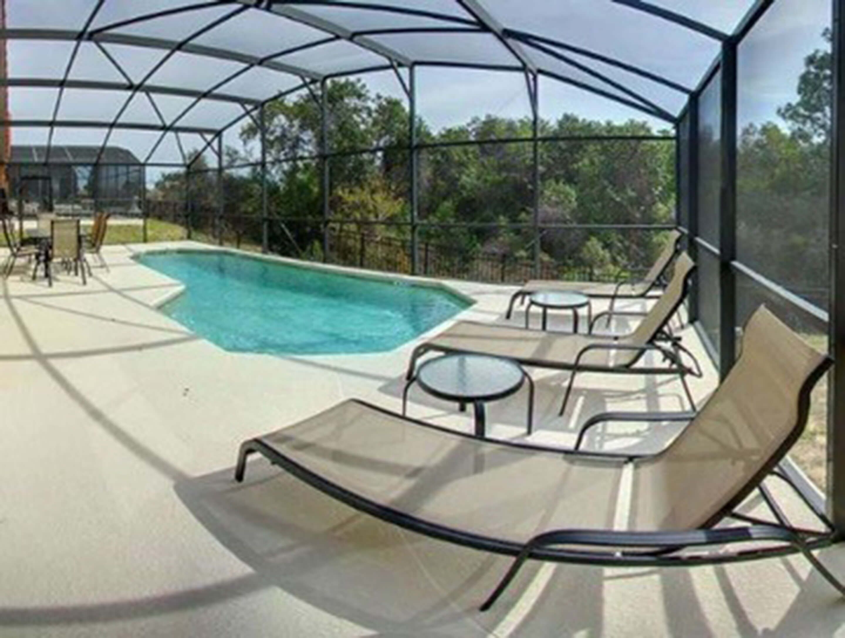 A covered outdoor swimming pool area with lounge chairs and tables.