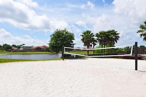 Una spiaggia sabbiosa con un campo da pallavolo e una rete, circondata da palme e da una distesa d'acqua.