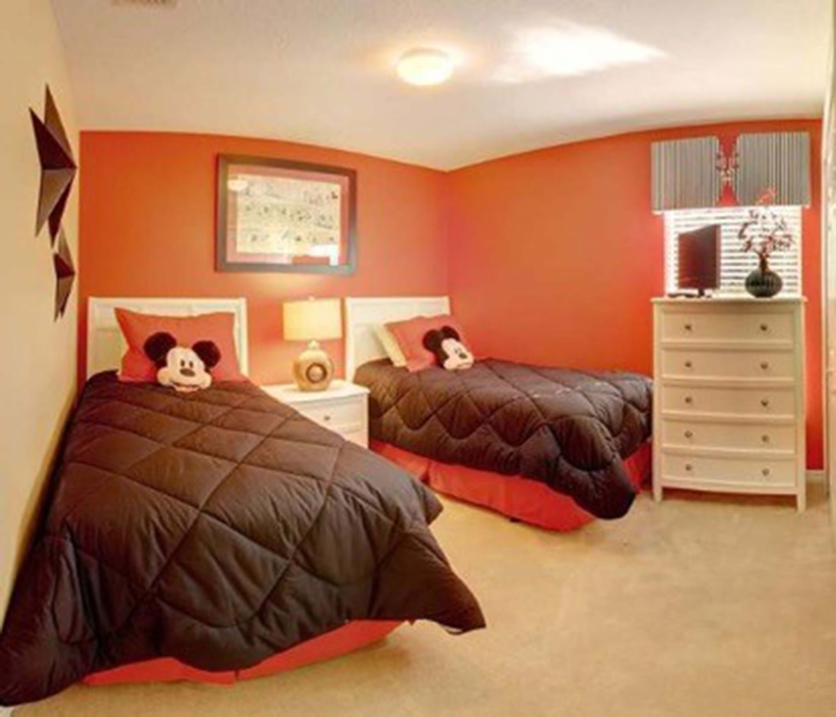 Une chambre avec deux lits, une commode et un coussin à l’effigie de Mickey Mouse.