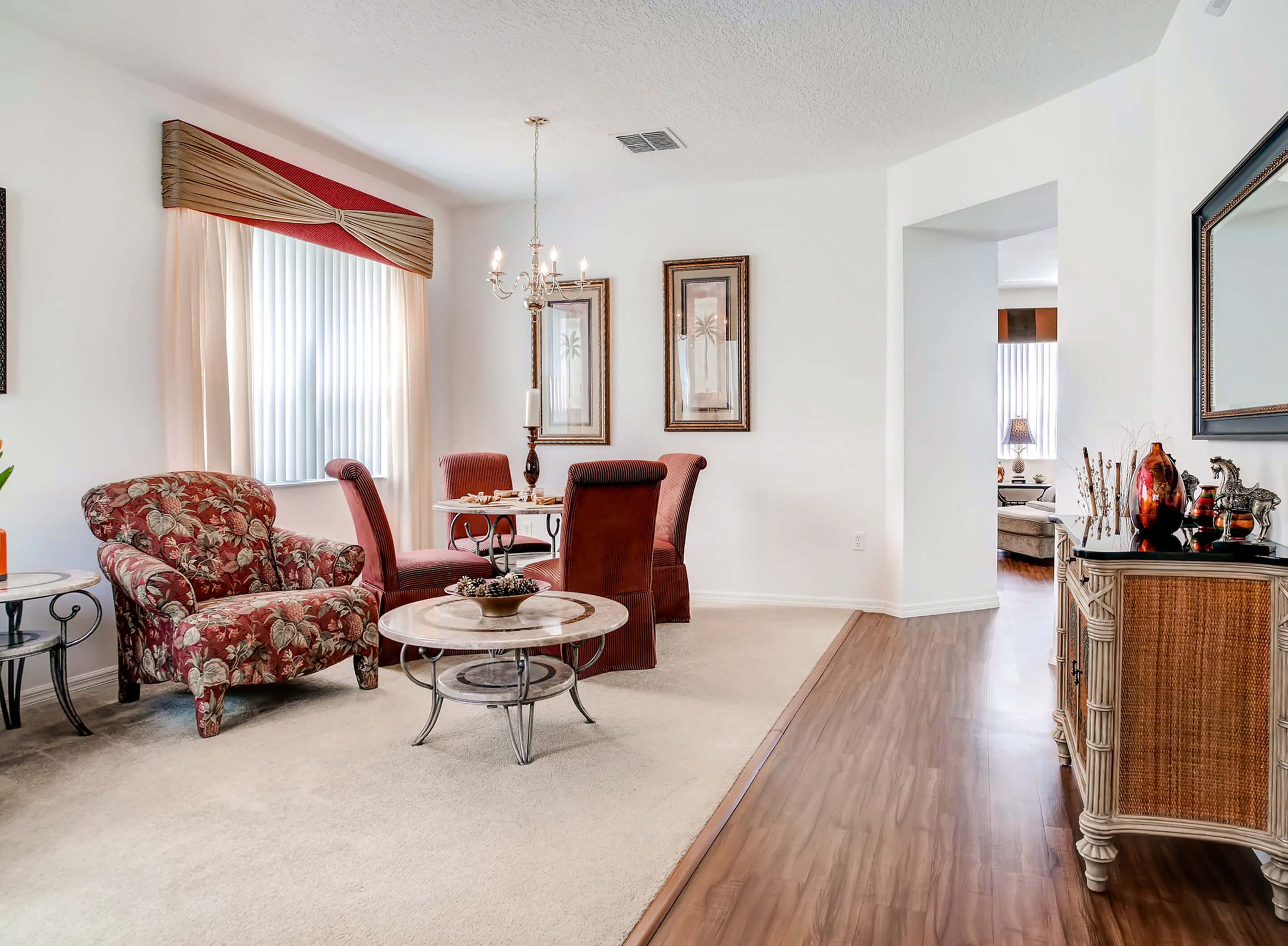 A living room with a red floral armchair, a round coffee table, and a dining area with red upholstered chairs.
