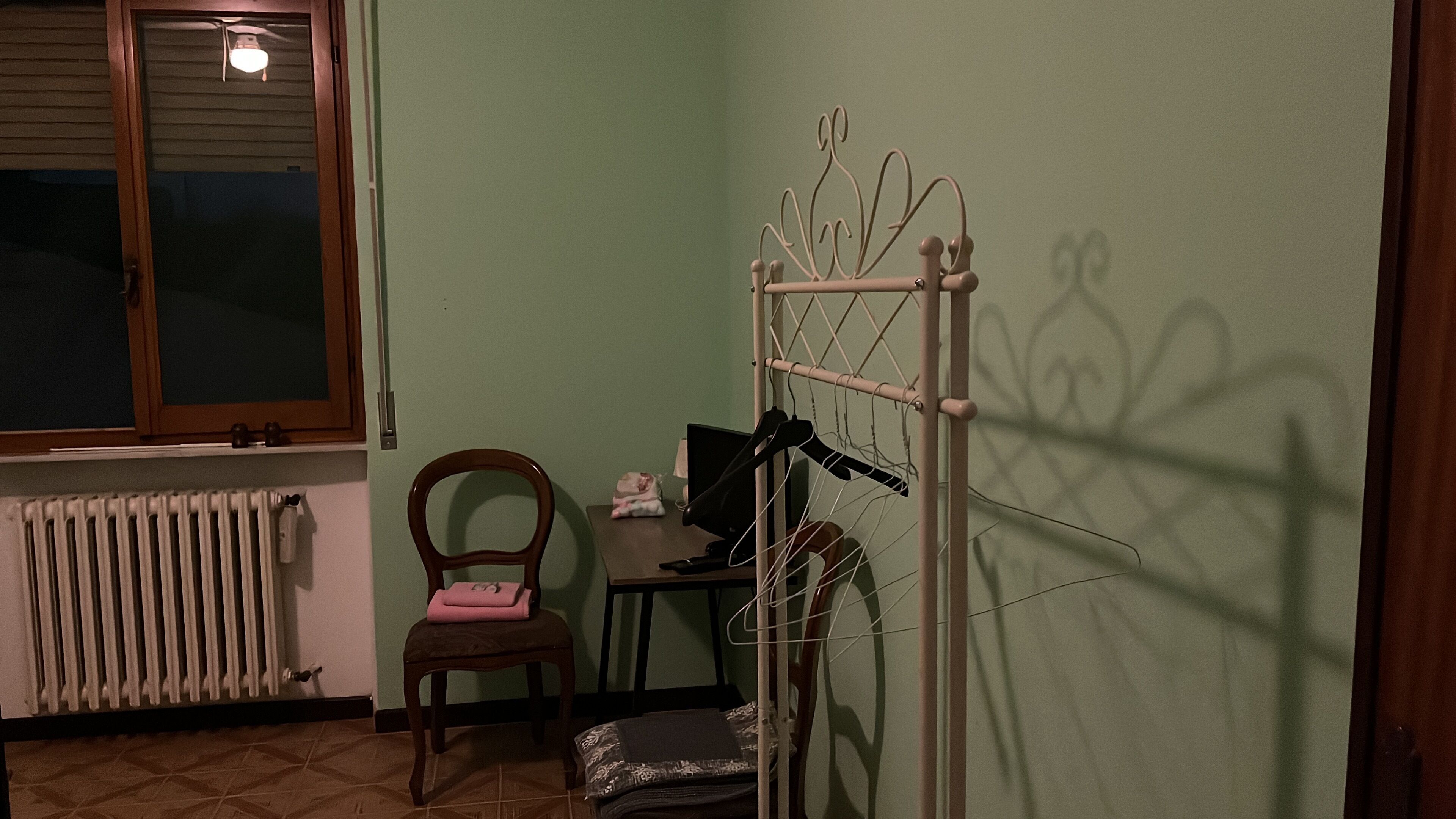 A room with a radiator, a chair, a desk with a computer, and a clothes drying rack.