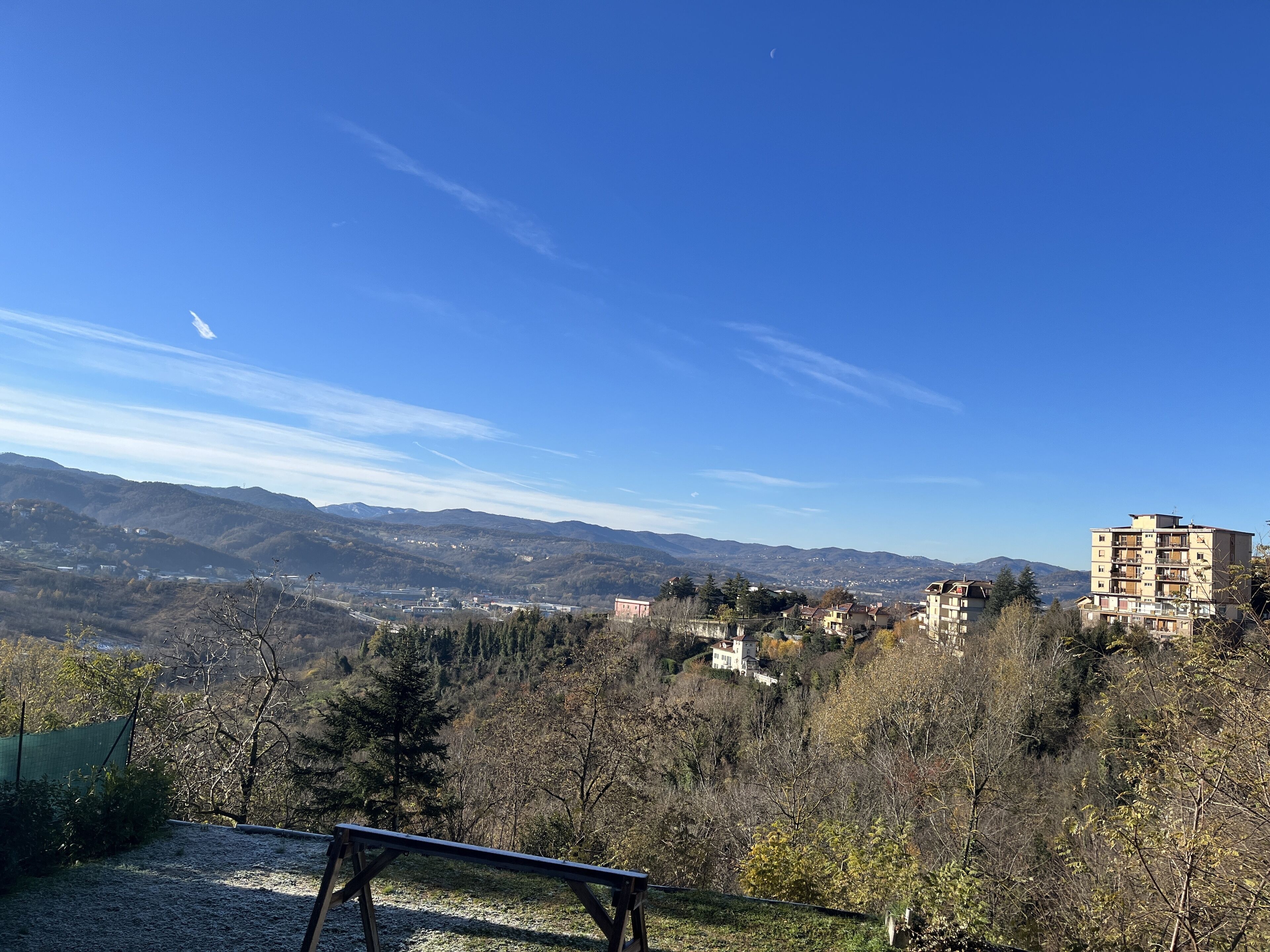 Une vue sur un paysage montagneux, avec un ciel dégagé, un banc au premier plan et un bâtiment à plusieurs étages en arrière-plan.