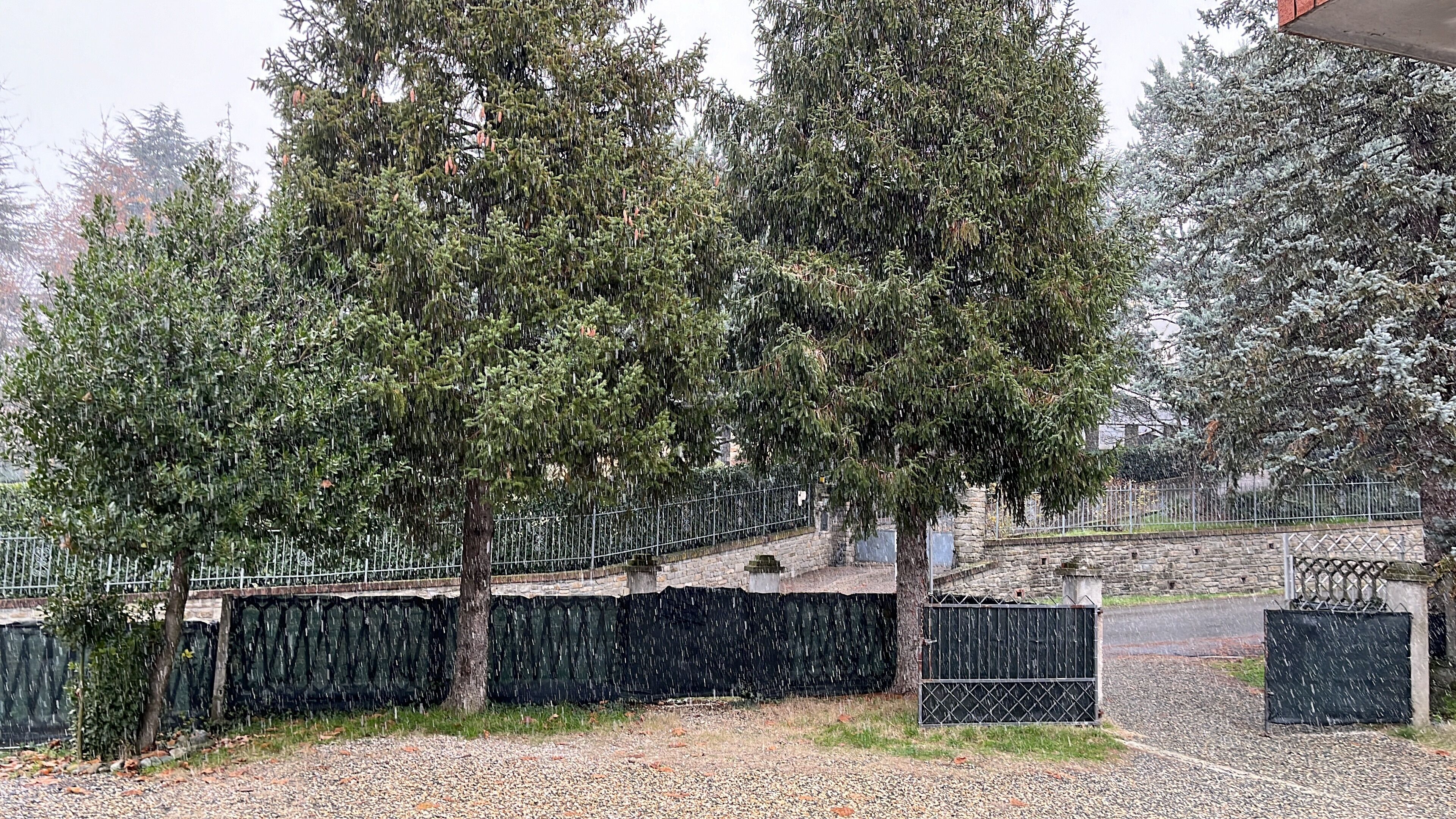 A gravel pathway leading to a stone bridge over a body of water, surrounded by trees and a metal fence.
