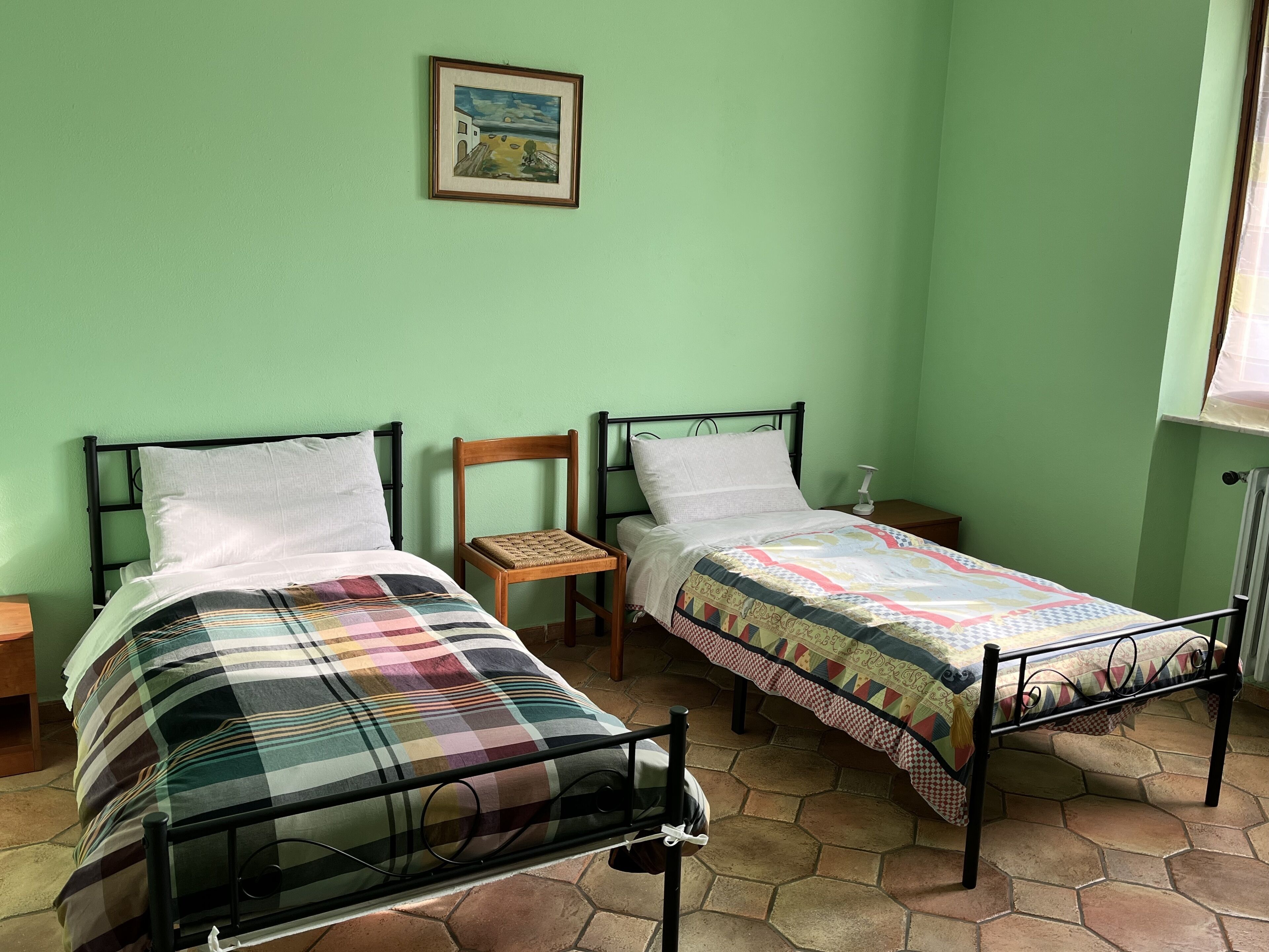 A room with two beds, a wooden chair, a nightstand, and a framed picture on the wall.