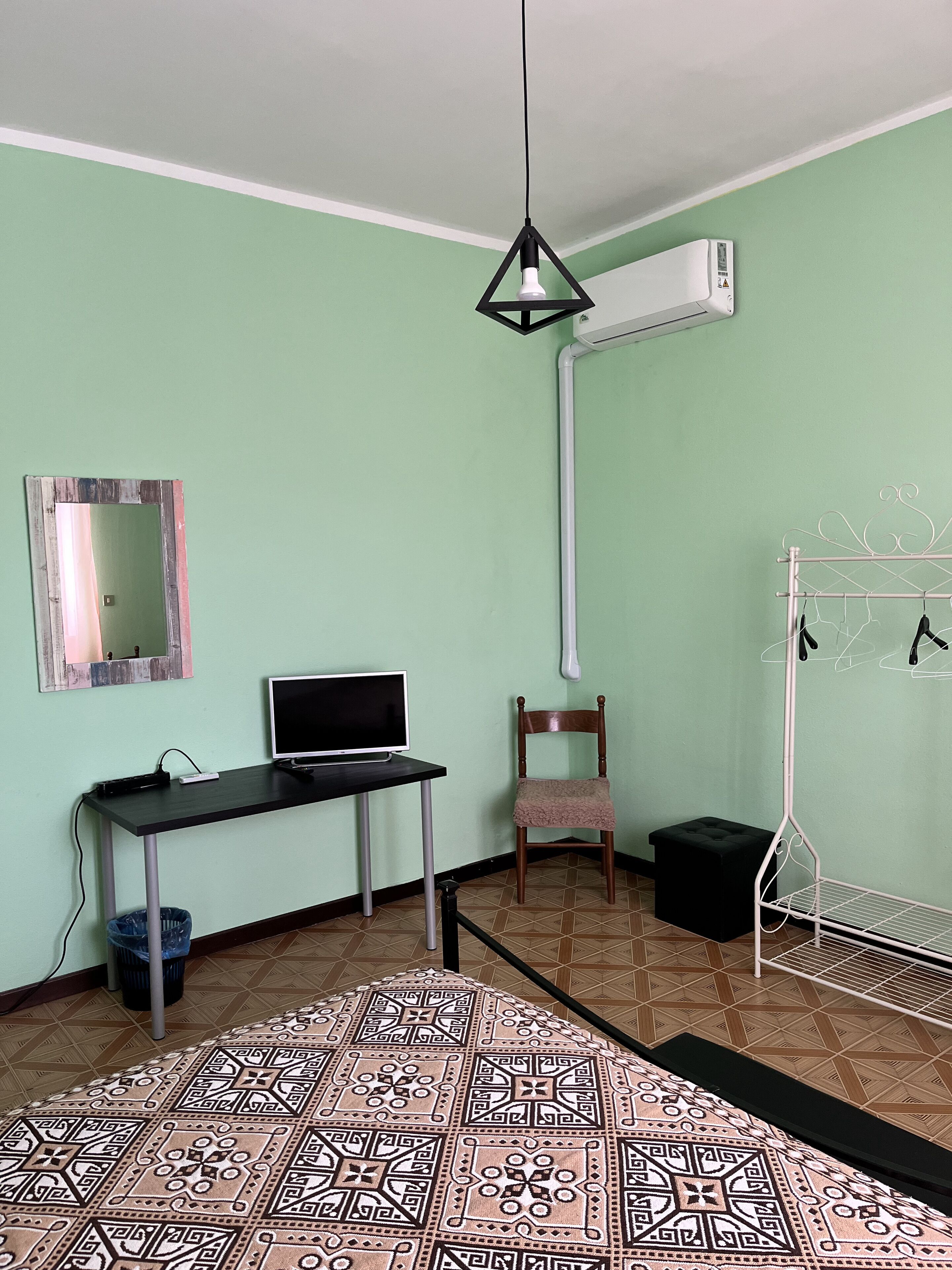 A room with a desk, chair, air conditioning unit, and a hanging light fixture.