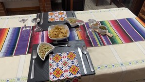 Una mesa de comedor dispuesta con platos, tazones y cubiertos, una chimenea al fondo y una silla.