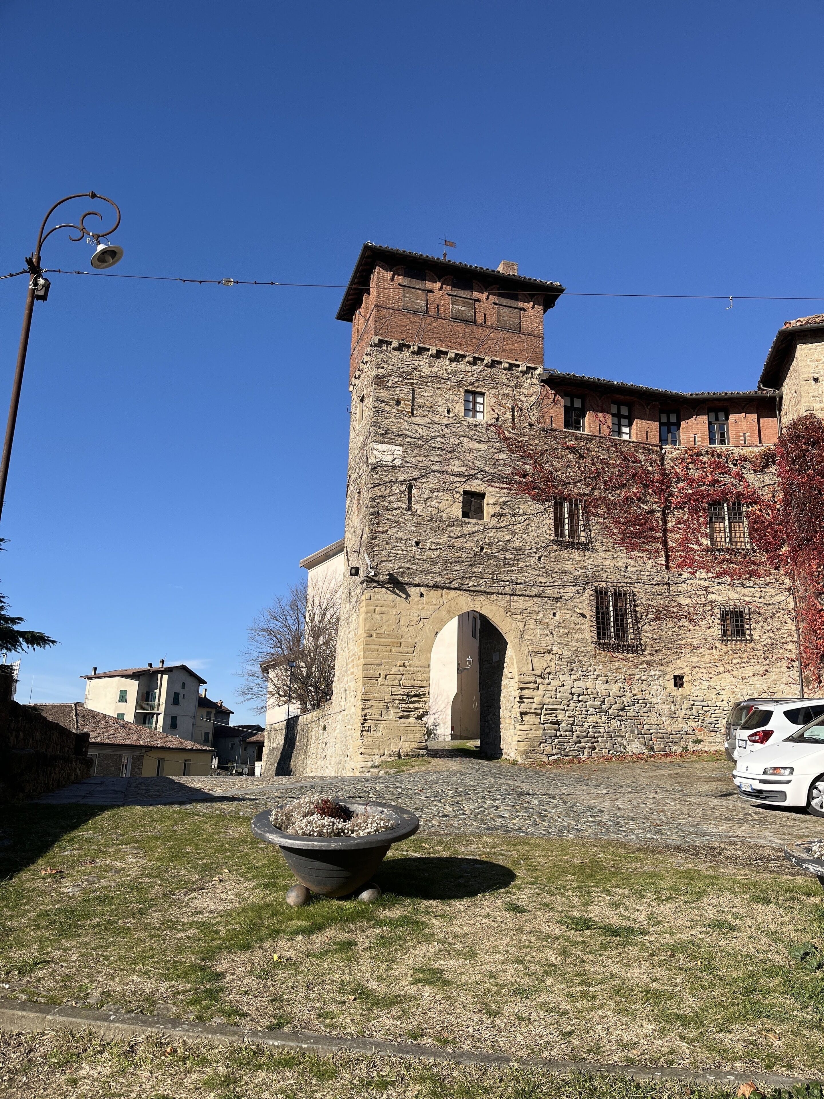 Un bâtiment historique en pierre, doté d’une entrée centrale en arc de cercle, d’une petite cour et d’une plante en pot au premier plan.