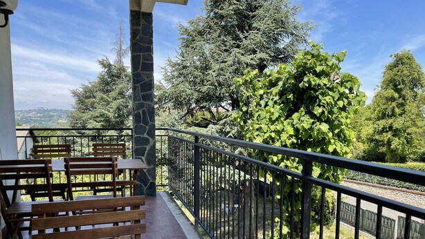Un balcón con bancos de madera y un pilar de piedra, con vista a un jardín con árboles y un muro de piedra.