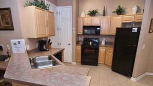 A kitchen with granite countertops, wooden cabinets, a black refrigerator, a stove, and a microwave. - Enchanted Retreat (Davenport)