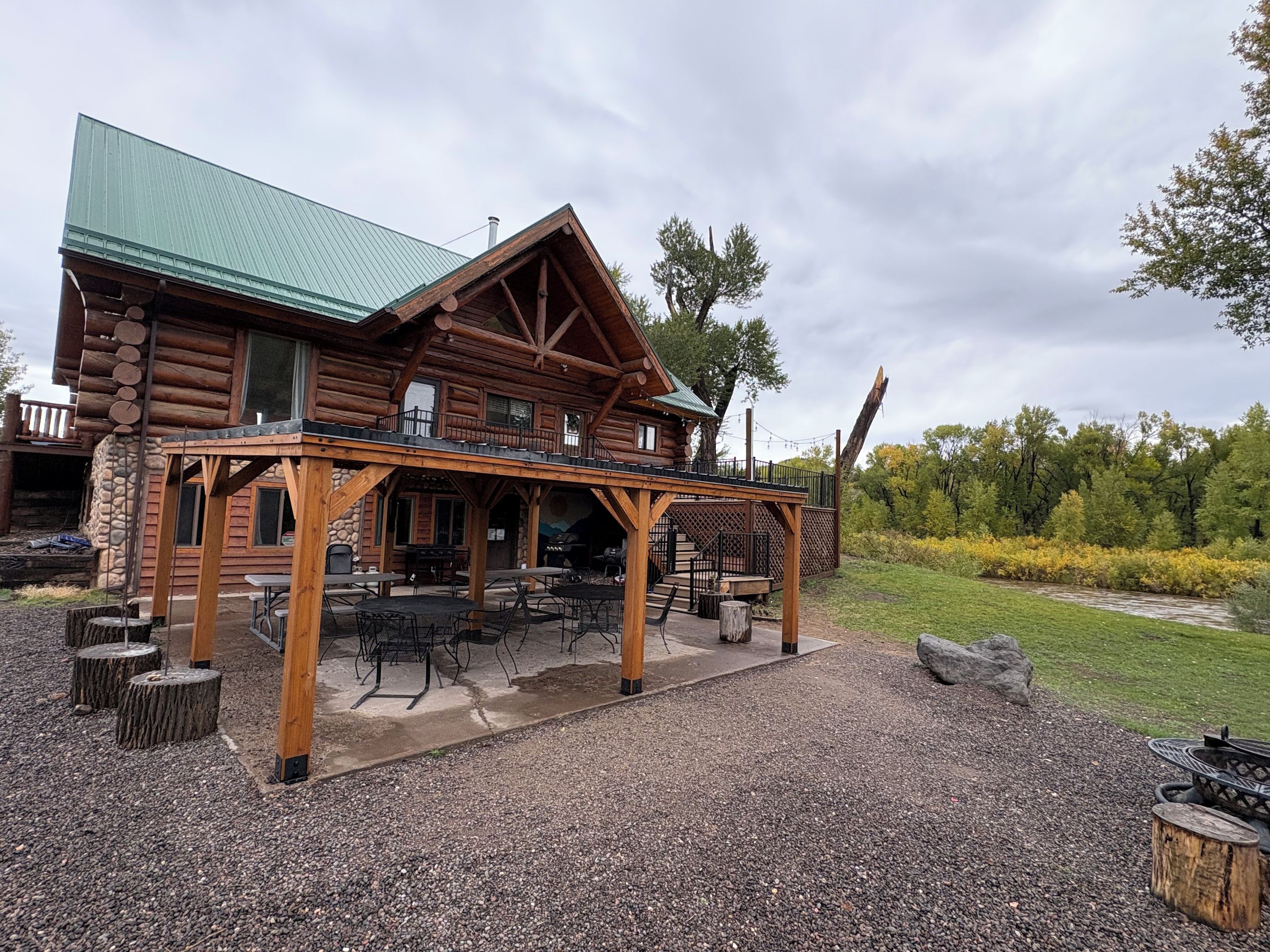 A log cabin with a covered patio, outdoor seating, and a stone foundation.