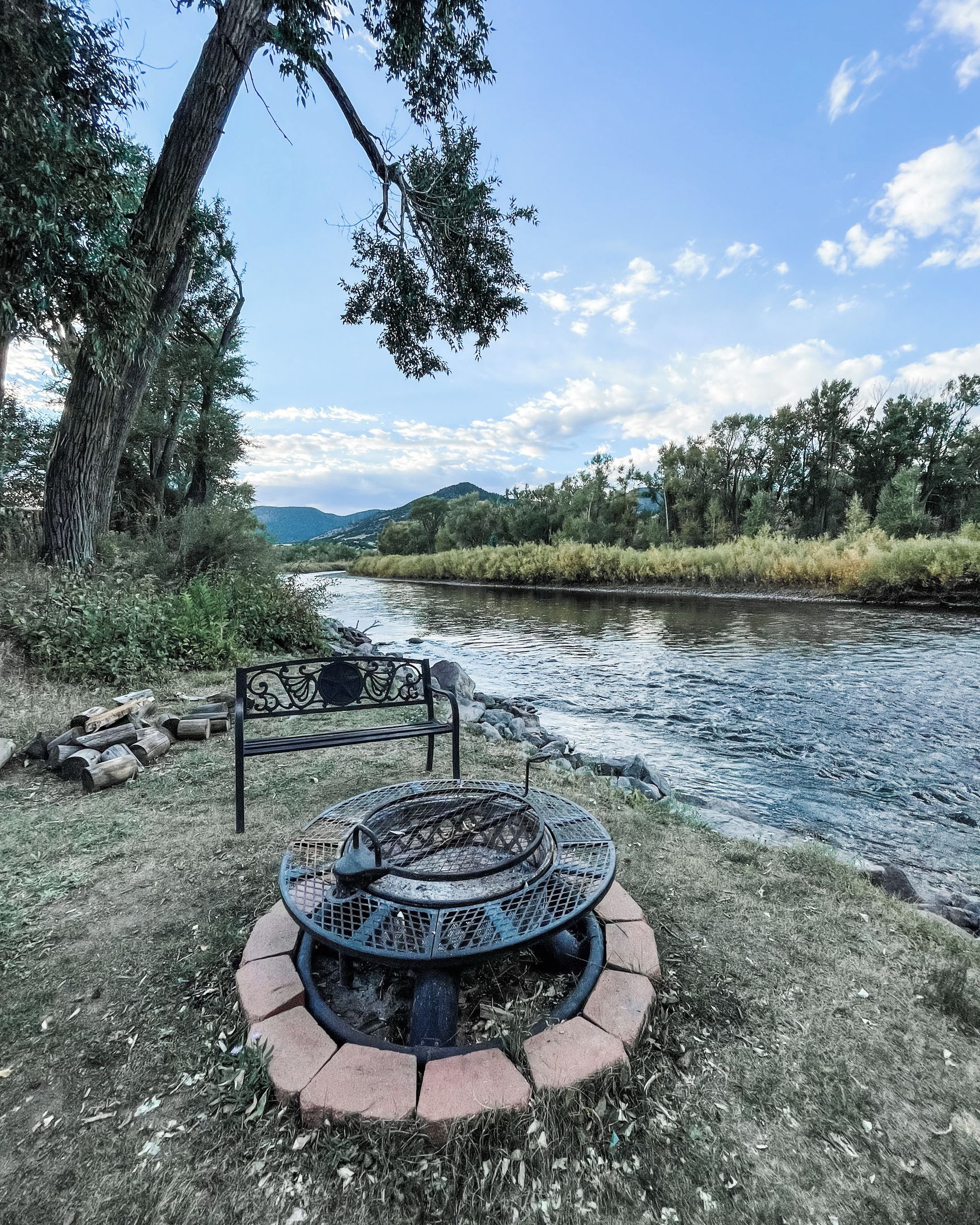 Un parc au bord de la rivière, équipé d’un foyer en métal et d’un banc.