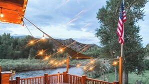 Una terrazza in legno con posti a sedere all'aperto, vista su un fiume e montagne.