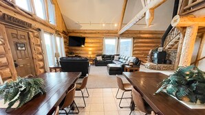 Interno di una baita di legno con zona pranzo, soggiorno con camino e televisore montato a parete.