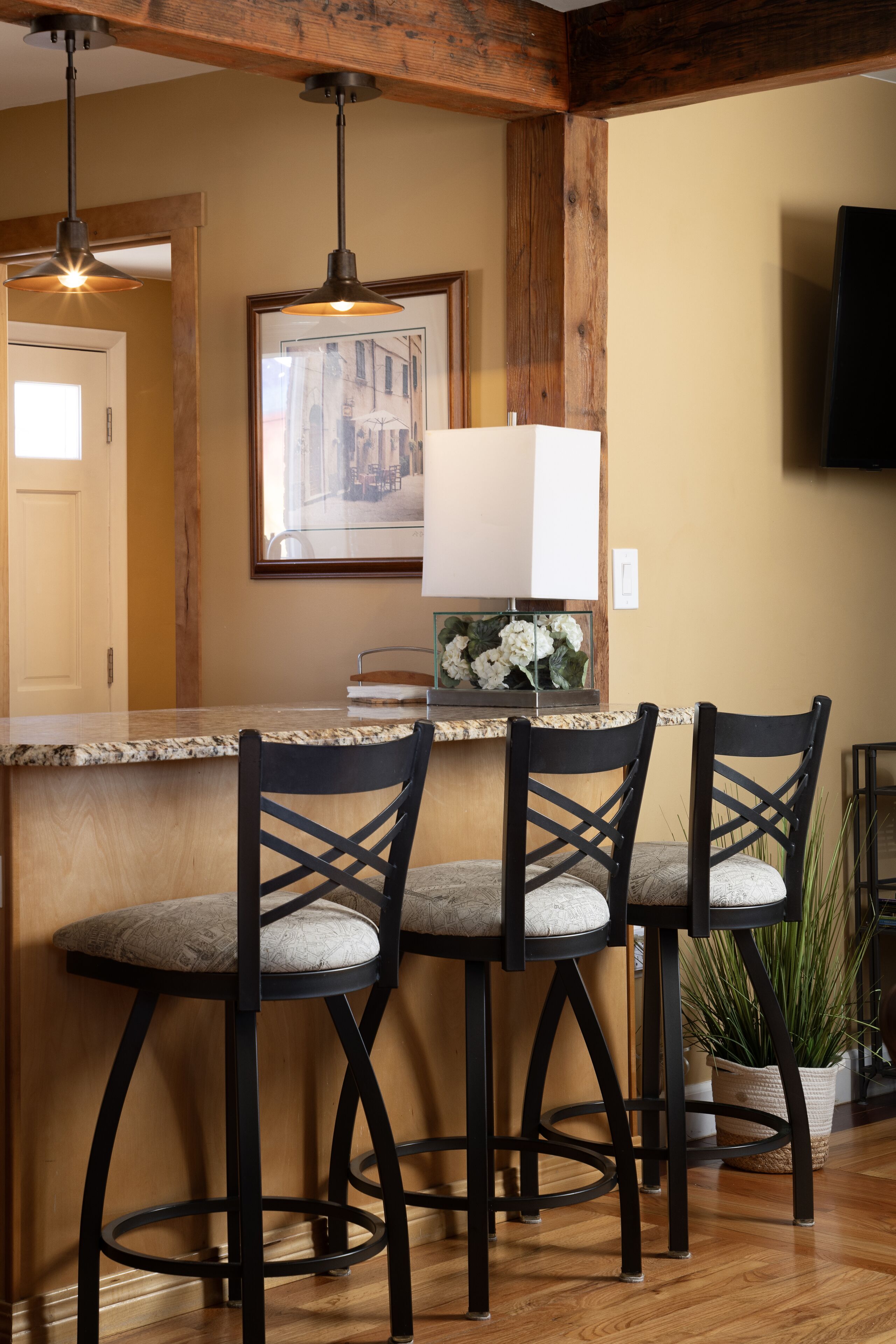 A kitchen with wooden beams, a granite countertop, and three bar stools with cushioned seats.
