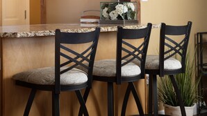 Una cocina con vigas de madera, encimera de granito y tres taburetes con asientos acolchados.