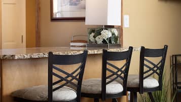 A kitchen with wooden beams, a granite countertop, and three bar stools with cushioned seats.