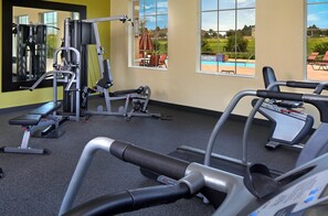 A gym with cardio equipment, weight machines, and a view of a swimming pool and outdoor seating. - Bella Vista Villa (Davenport)