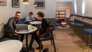 Een moderne zithoek met ronde tafels, barstoelen en kunstwerken in lijsten aan de wanden.