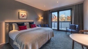 Een hotelkamer met een groot bed, een bureau, een stoel en een balkon met uitzicht op de stad.