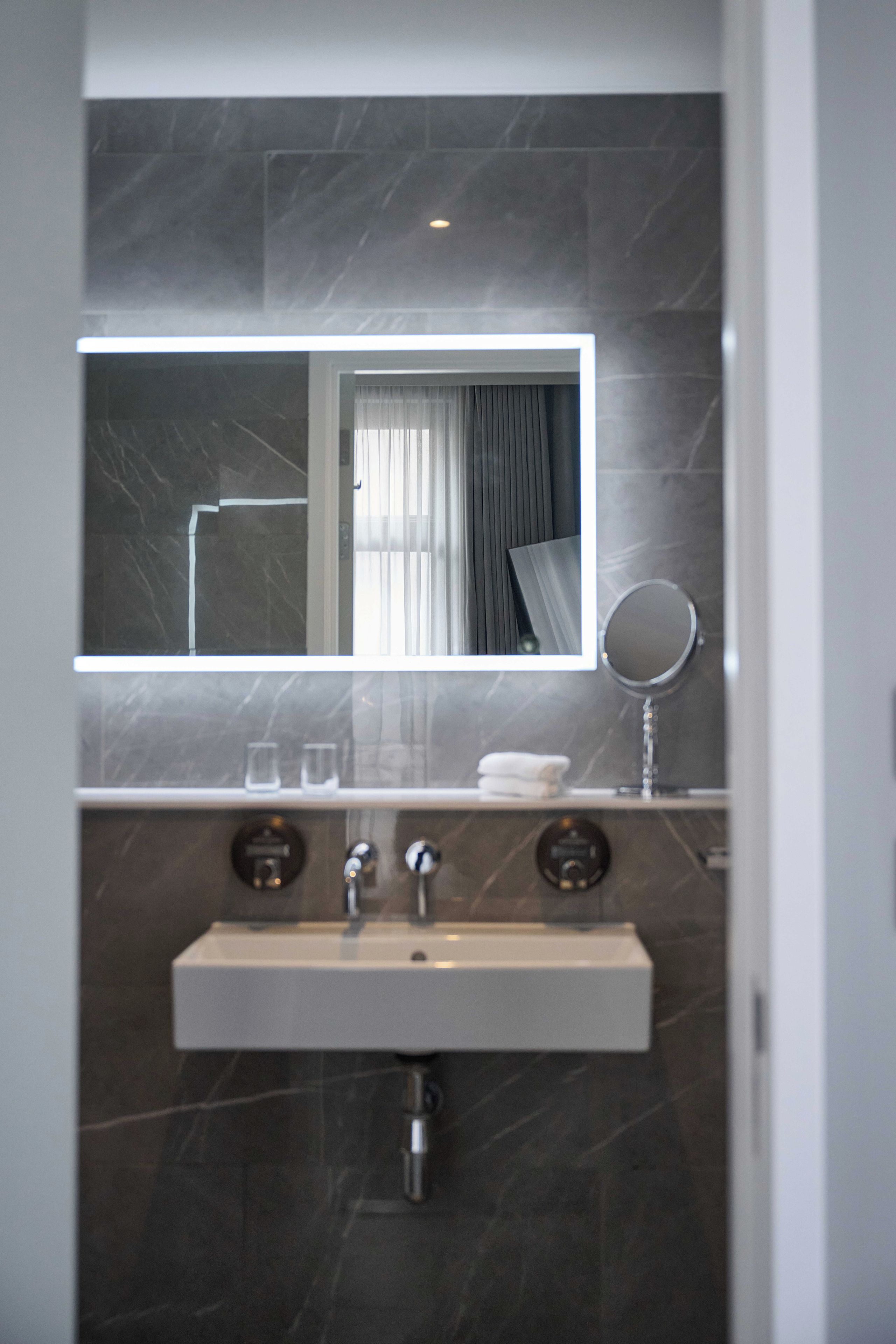 A modern bathroom with a marble sink, a mirror, and a towel rack.