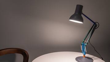 A desk lamp with a curved neck and a round base, positioned on a white table against a grey wall.