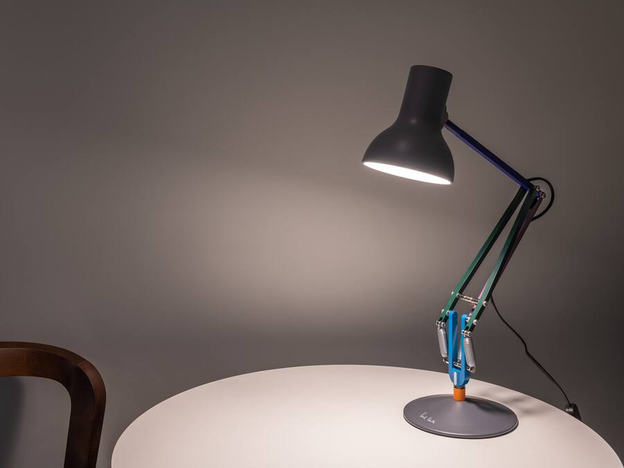 A desk lamp with a curved neck and a round base, positioned on a white table against a grey wall.