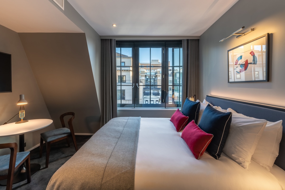 A hotel room with a large bed, a desk, and a window with a city view.