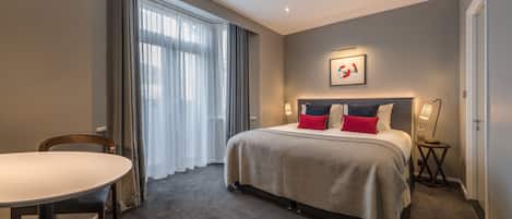A modern hotel room with a large bed, a dining table, and a view of the city.
