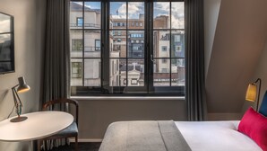 Een hotelkamer met een bed, een bureau, een stoel en een groot raam met uitzicht op de stad.