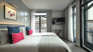 Une chambre d’hôtel avec un grand lit, une télévision et un balcon donnant sur les bâtiments.