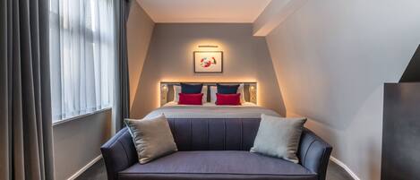 A hotel room with a bed, a sofa, and a large window with curtains.