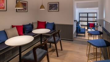 A modern dining area with a long bench, two round tables, and blue chairs.